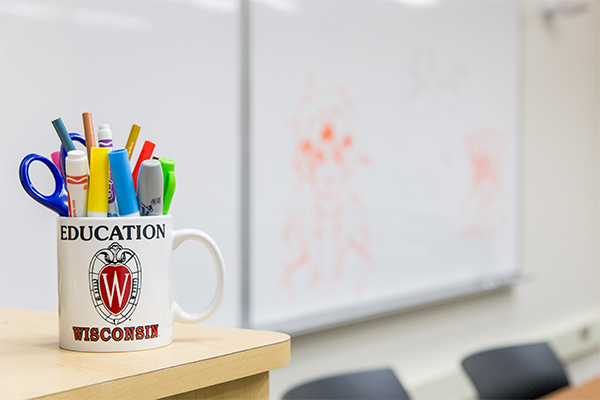 mug with "education" text full of pens and markers in front of whiteboard
