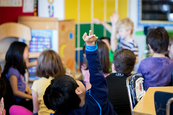 classroom with a group of children and one raising his hand